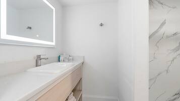 A bathroom with a white sink, mirror, and marble shower.