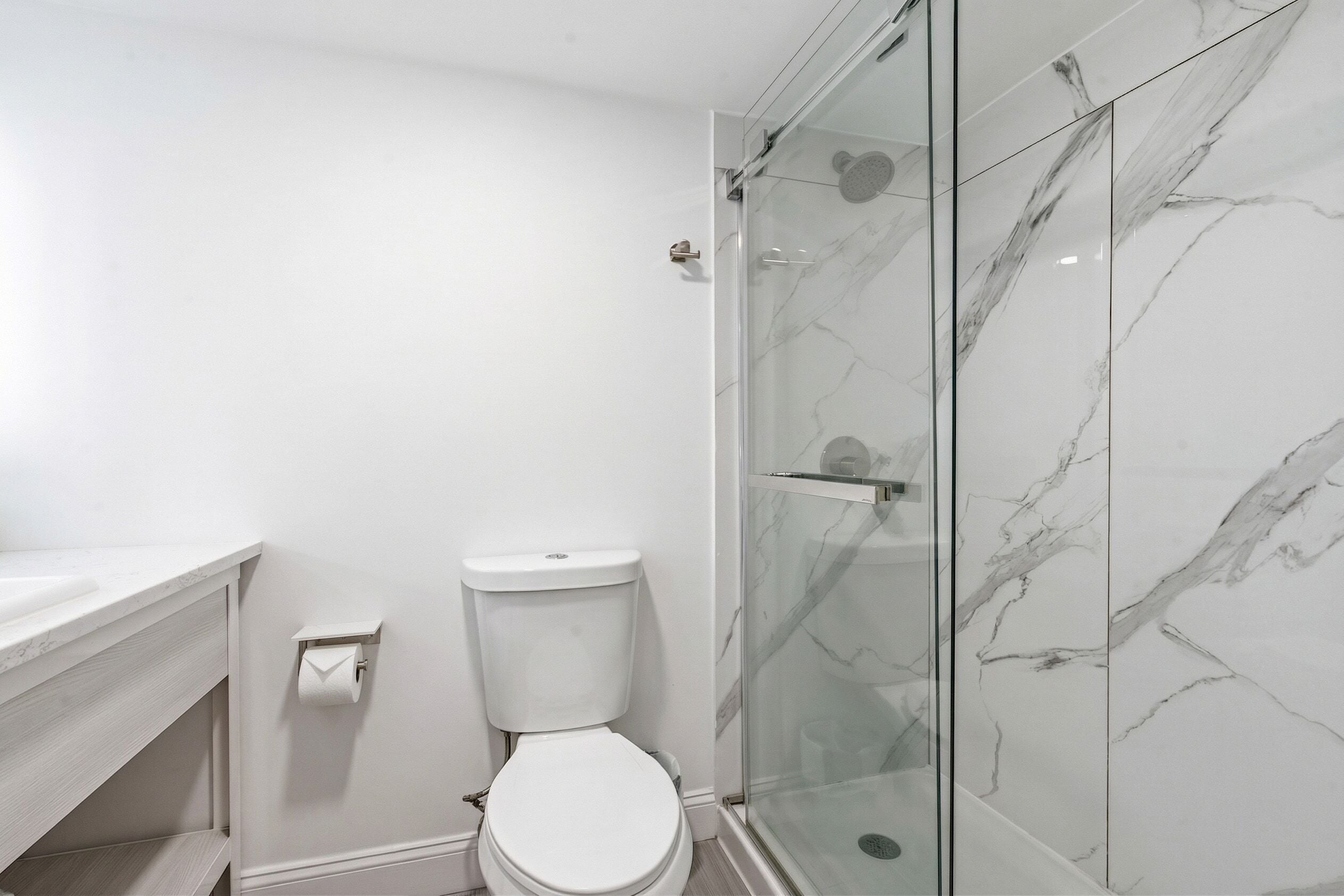 Un baño con inodoro, cabina de ducha de vidrio y pared de mármol.