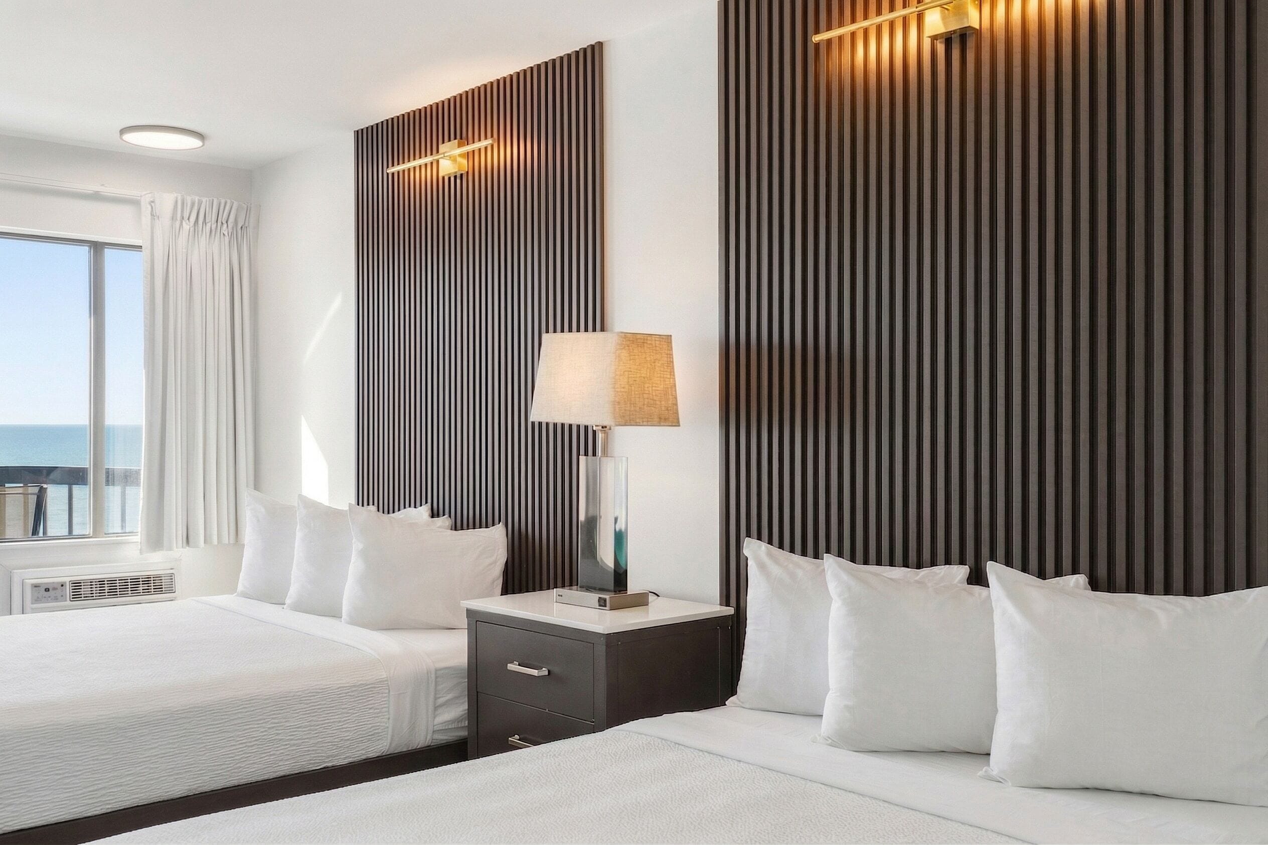 Une chambre d’hôtel moderne avec un grand lit, une table de chevet avec une lampe, un téléviseur fixé au mur et une fenêtre avec des rideaux.
