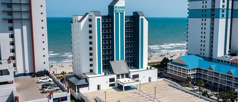 A hotel with a parking lot, a beach view, and a sign reading "GRAND BEACH".