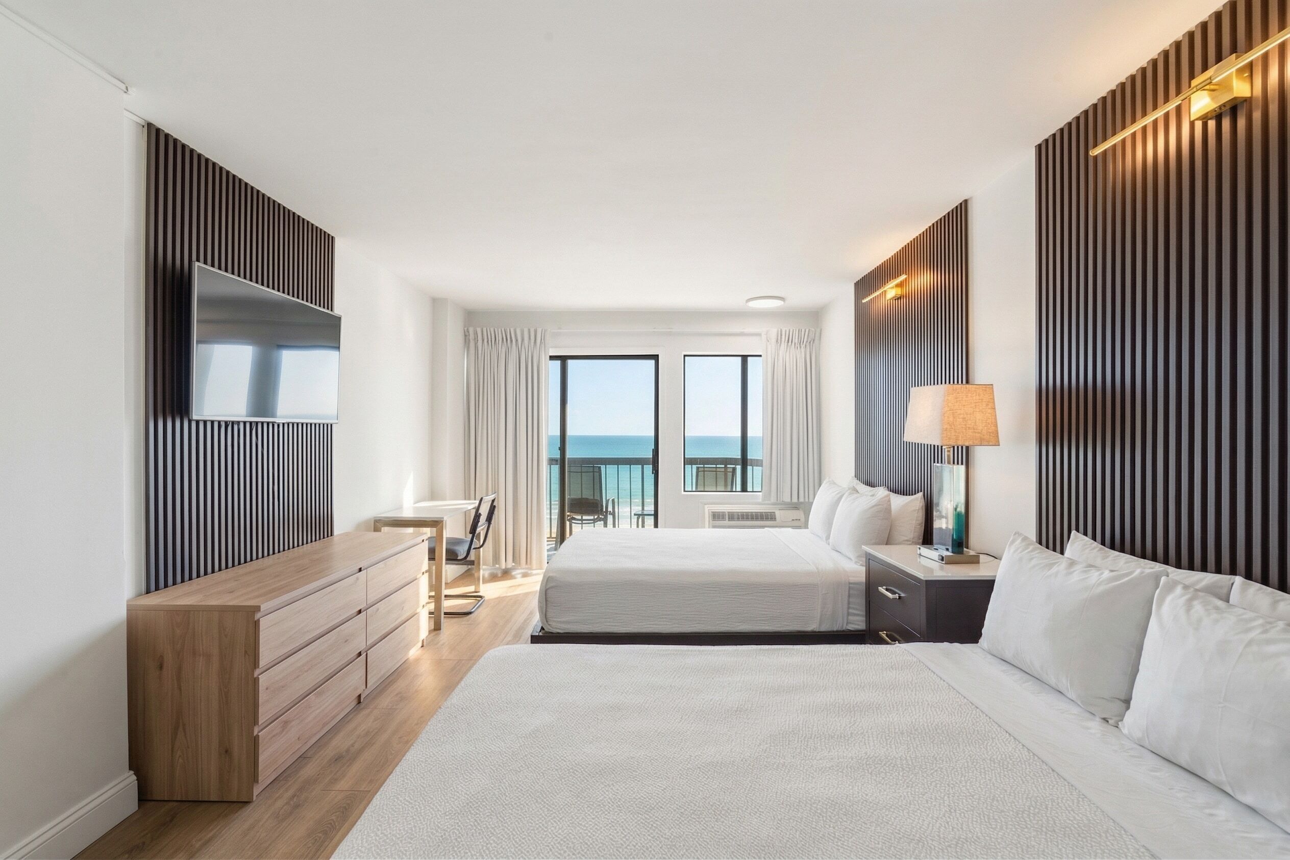 A hotel room with a large bed, a desk, a chair, a TV, and a view of the sea.