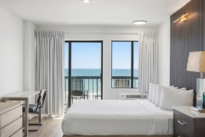 Habitación de hotel con cama, escritorio, silla, televisor y balcón con vista al mar.