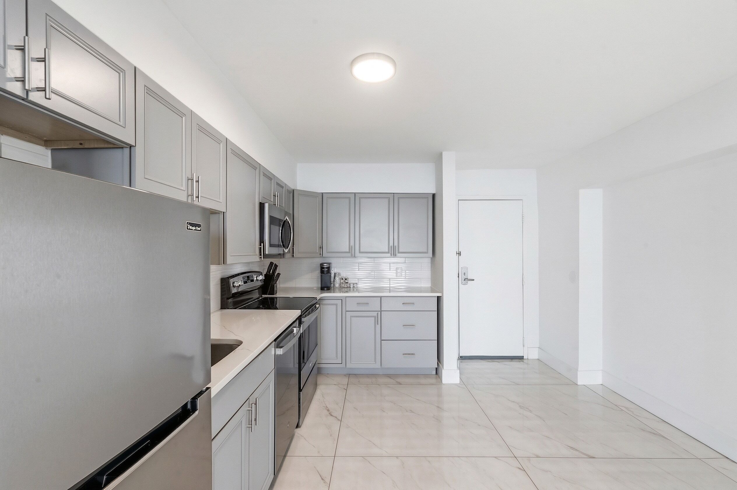 A modern kitchen with grey cabinets, stainless steel appliances, and a tiled floor.