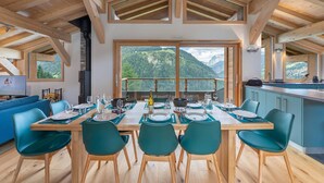 A dining area with a table set for four, large windows offering a mountain view, and a kitchen area with a view of the mountains. - Duplex flat for 10 people near Lac de Vonnes (CHATEL)