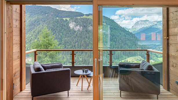 A modern room with a wooden floor, two dark sofas, a small round table, and a glass door leading to a balcony with a mountain view. - Duplex flat for 10 people near Lac de Vonnes (CHATEL)