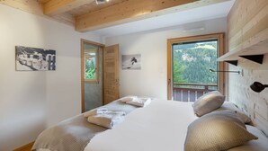 A bedroom with a bed, a wooden ceiling, a window with a view of trees, and a door leading outside. - Duplex flat for 10 people near Lac de Vonnes (CHATEL)