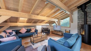 A modern loft-style living room with exposed wooden beams, a stone fireplace, and large windows offering a view of the outdoors. - Duplex flat for 10 people near Lac de Vonnes (CHATEL)