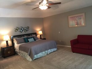 A bedroom with a bed, two bedside lamps, a ceiling fan, a red couch, and a wall decoration.
