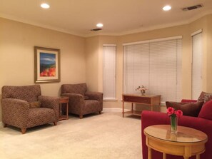 Una sala de estar con dos sillones, un sofá rojo, una mesa de centro de vidrio y un cuadro en la pared.