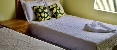 A double bed with a wooden headboard, two pillows with a lemon pattern, and a white blanket.