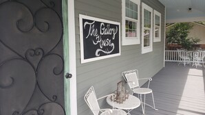 A porch with a sign reading "The Bakery House," white metal chairs, and a small table with bottles. - The Gallery House Bed & Breakfast (Stephenville)