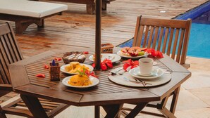 A wooden deck with a table set for a meal, a pool in the background, and lounge chairs. - Pousada Villa Bella (Itacaré)