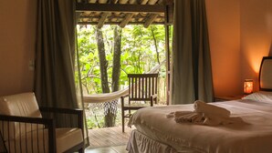 A bedroom with a bed, a chair, a hammock, and a view of greenery through a window. - Pousada Villa Bella (Itacaré)