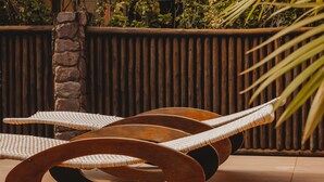 A lounge chair with a woven seat and backrest, placed on a wooden floor with a stone pillar nearby. - Pousada Villa Bella (Itacaré)