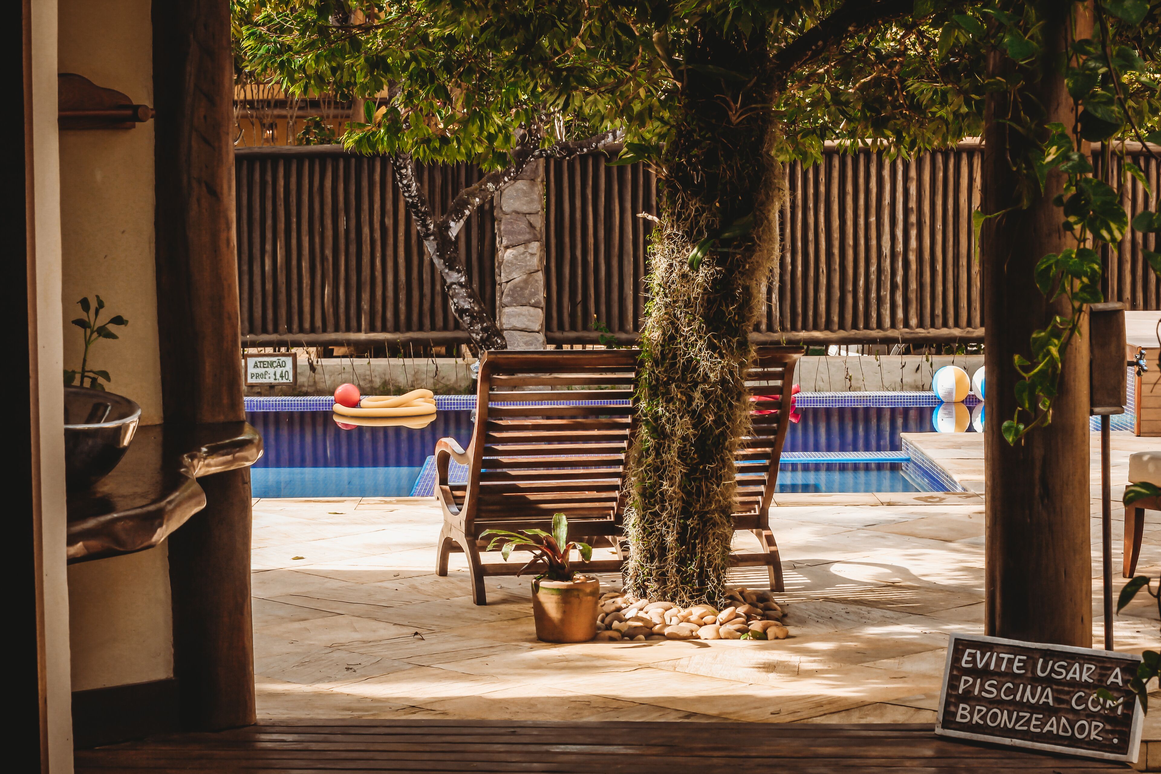 Zona de piscina con bancos de madera, una planta en maceta y un letrero.