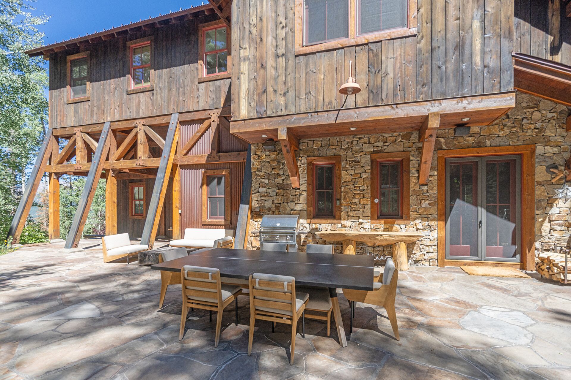 A wooden cabin with a stone exterior, a stone patio, and a barbecue area.