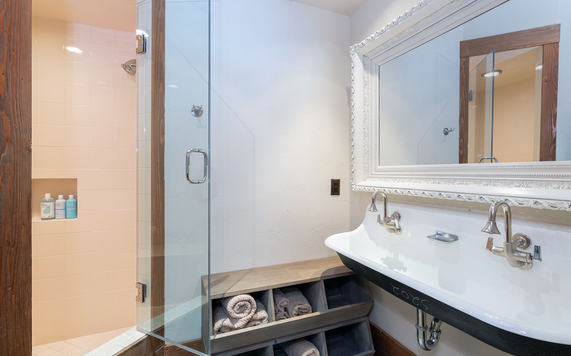 A modern bathroom with a glass shower enclosure, a white sink with a black countertop, and a large mirror with an ornate frame.