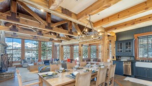 A rustic wooden interior with a dining area, kitchen, and large windows offering mountain views. - Luxury Home | Hot Tub, Decks + Sweeping Mountain views (Mountain Village)