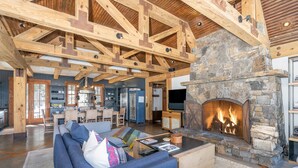 A spacious living room with a stone fireplace, wooden beams, and a modern sofa. - Luxury Home | Hot Tub, Decks + Sweeping Mountain views (Mountain Village)