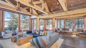 A spacious living room with large windows, wooden beams, and a mix of seating areas including sofas and a coffee table. - Luxury Home | Hot Tub, Decks + Sweeping Mountain views (Mountain Village)