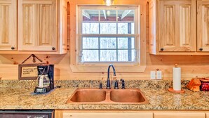 A kitchen with wooden cabinets, a granite countertop, a double sink, a coffee maker, and a window with a view of trees. - Pet-Friendly Ellijay Escape w/ Yard & Grill! (Ellijay)