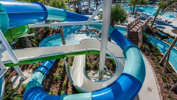A water park with multiple slides and pools, surrounded by palm trees and lounge areas. - Refined stay Disney Theme 8BR Resort Villa With FREE Heated Pool/Spa Near Disney (Davenport)