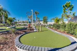 A golf course with a putting green, surrounded by landscaped areas and palm trees.
