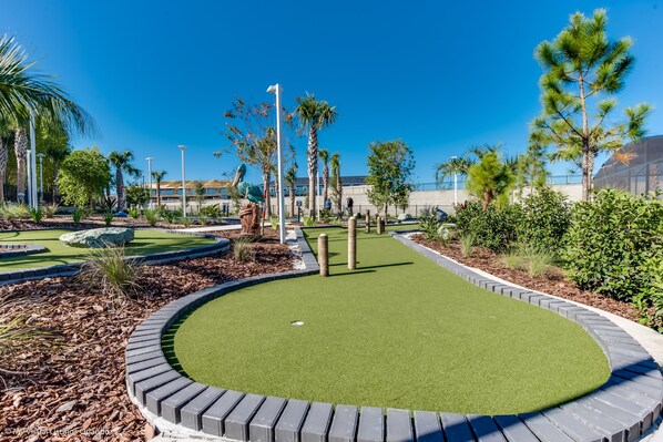 A well-maintained mini-golf course with a circular layout, surrounded by landscaped areas and palm trees.