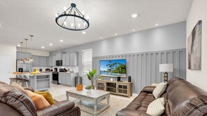 A modern living room with a brown leather sofa, a coffee table, and a TV on a wooden stand. - Refined stay Disney Theme 8BR Resort Villa With FREE Heated Pool/Spa Near Disney (Davenport)