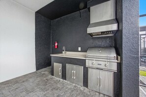 Une cuisine d’extérieur compacte, dotée d’un barbecue intégré, d’un évier et de placards de rangement.