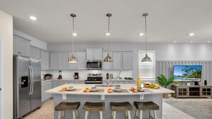 A modern kitchen with a central island, stainless steel appliances, pendant lighting, and a large window with blinds. - Refined stay Disney Theme 8BR Resort Villa With FREE Heated Pool/Spa Near Disney (Davenport)