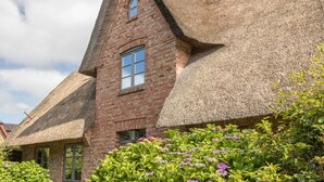 A traditional brick building with a steeply pitched thatched roof and a window. - House Hansen Hus, Germany (Sylt)