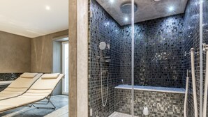 A modern bathroom with a glass-enclosed shower, a beige sun lounger, and a tiled mosaic wall. - House Hansen Hus, Germany (Sylt)