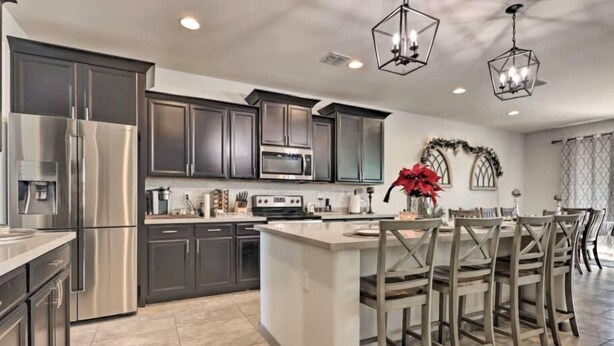 A modern kitchen with dark cabinets, stainless steel appliances, and a central island with chairs. - A home that feels like home, w/hot tub and spacious living room (San Tan Valley)