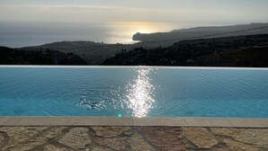 Una piscina con borde de baldosas de piedra, cielo despejado y atardecer al fondo.