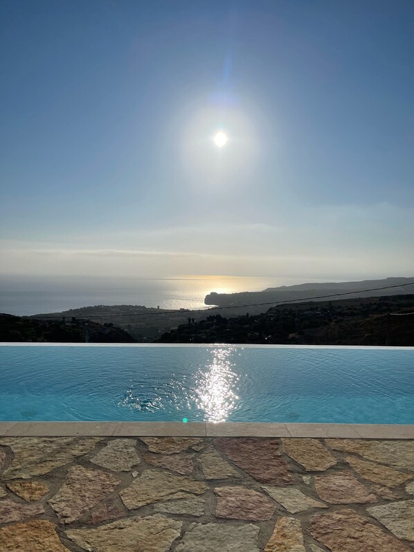 A swimming pool with a stone-tiled edge, a clear sky, and a sunset in the background.