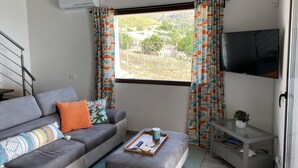 Una sala de estar moderna con un sofá gris, cortinas coloridas, un televisor de pantalla plana y una mesita con una bandeja.