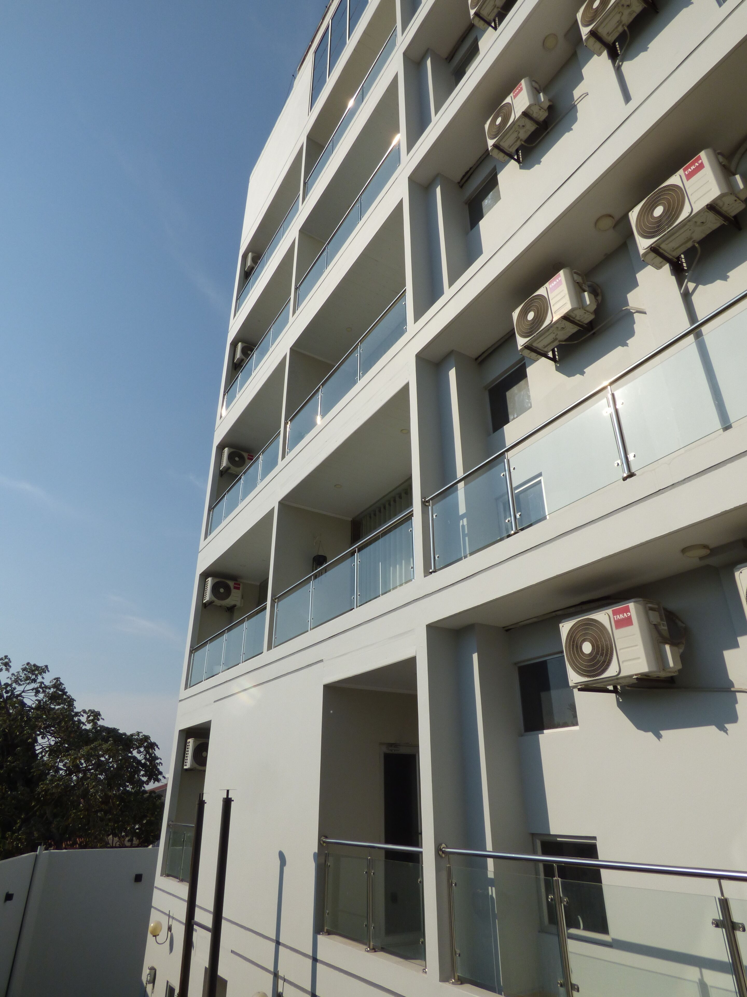 Un immeuble à plusieurs étages doté de balcons, de climatiseurs et surplombant un ciel dégagé.