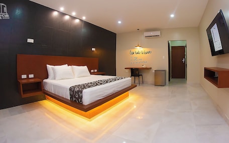 A hotel room with a large bed, bedside tables, a desk with a chair, a small refrigerator, and a TV mounted on the wall.
