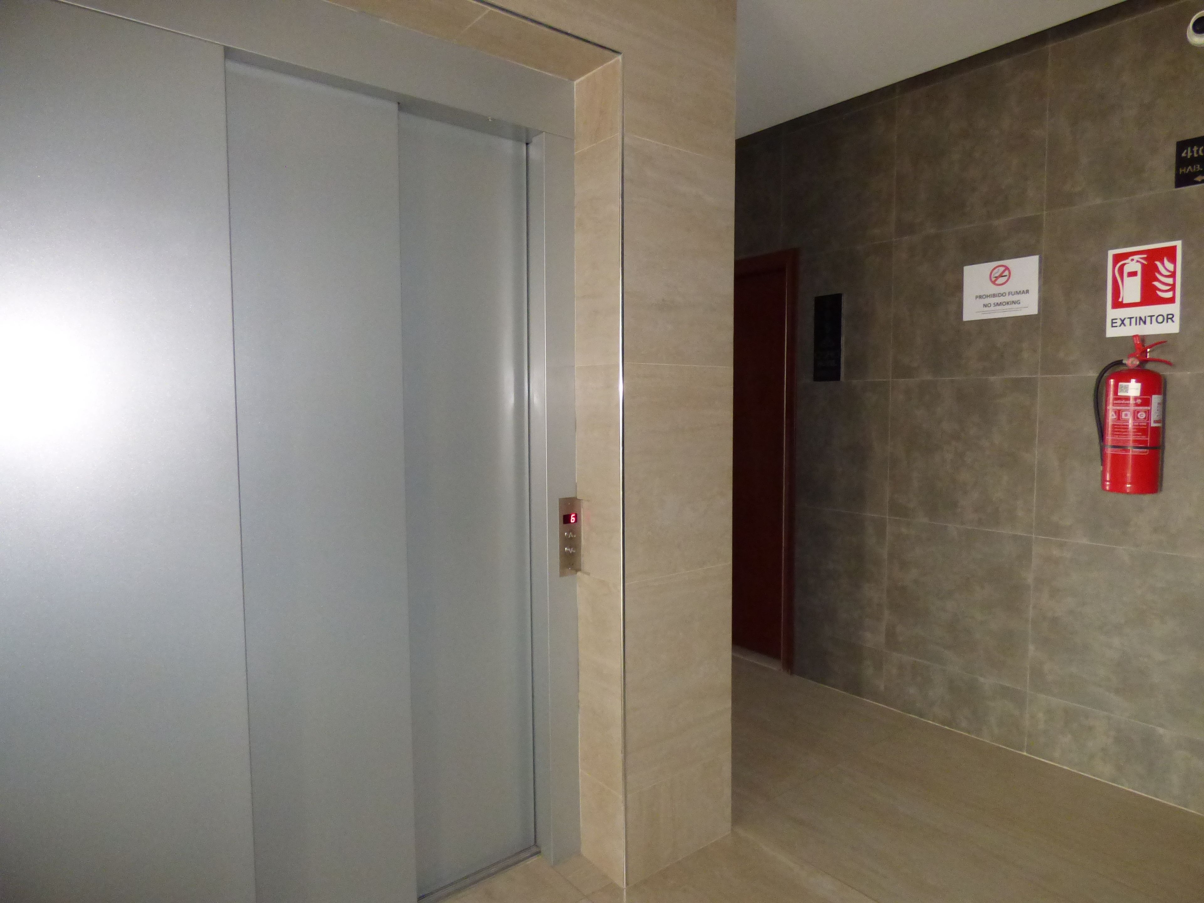 Un pasillo con extintor, señal de prohibido fumar y aviso de que el ascensor está fuera de servicio.