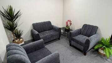A room with three grey sofas, a small table with a vase of flowers, and potted plants.