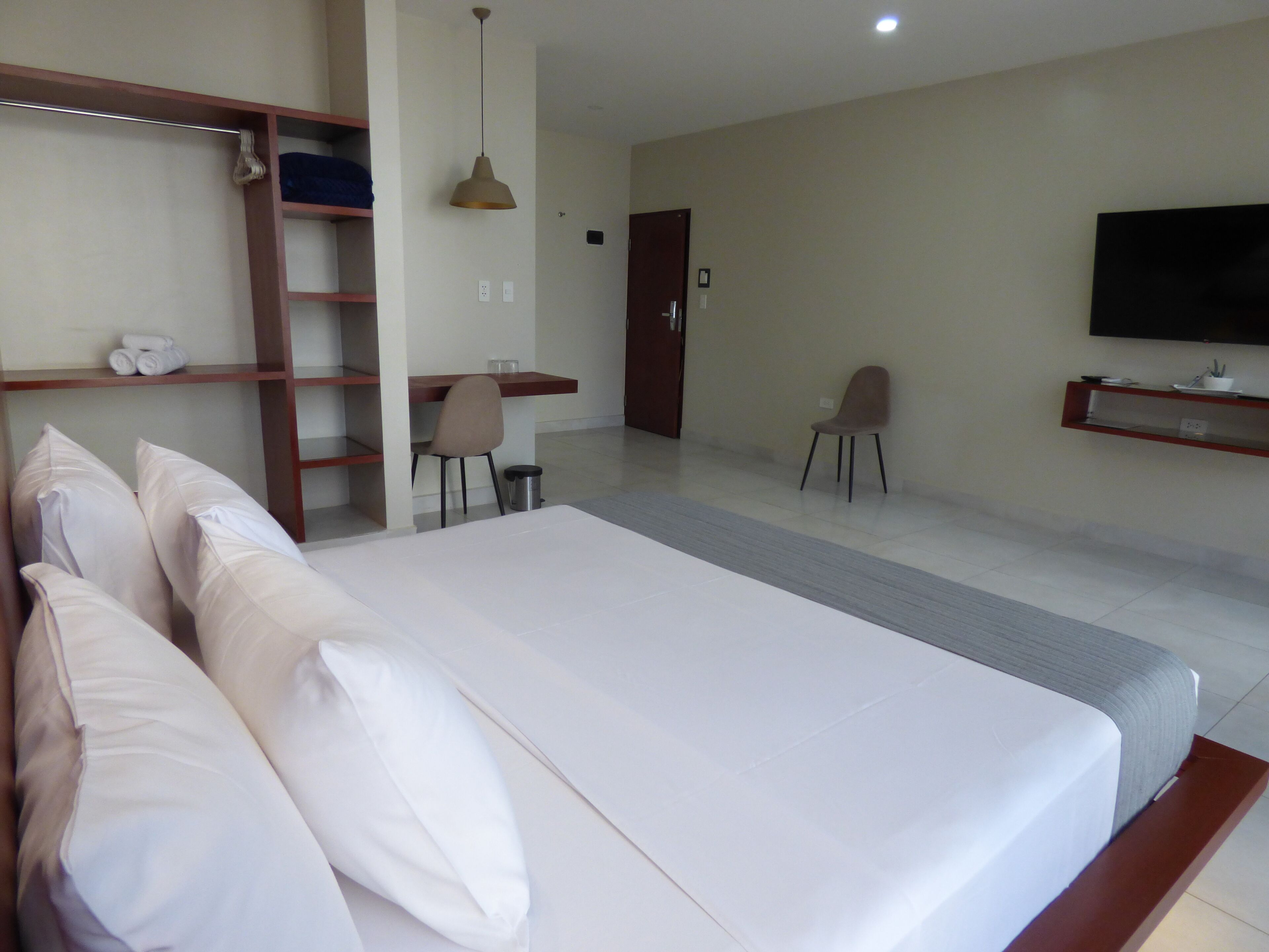 A hotel room with a bed, a desk, a chair, a TV, and a wardrobe.