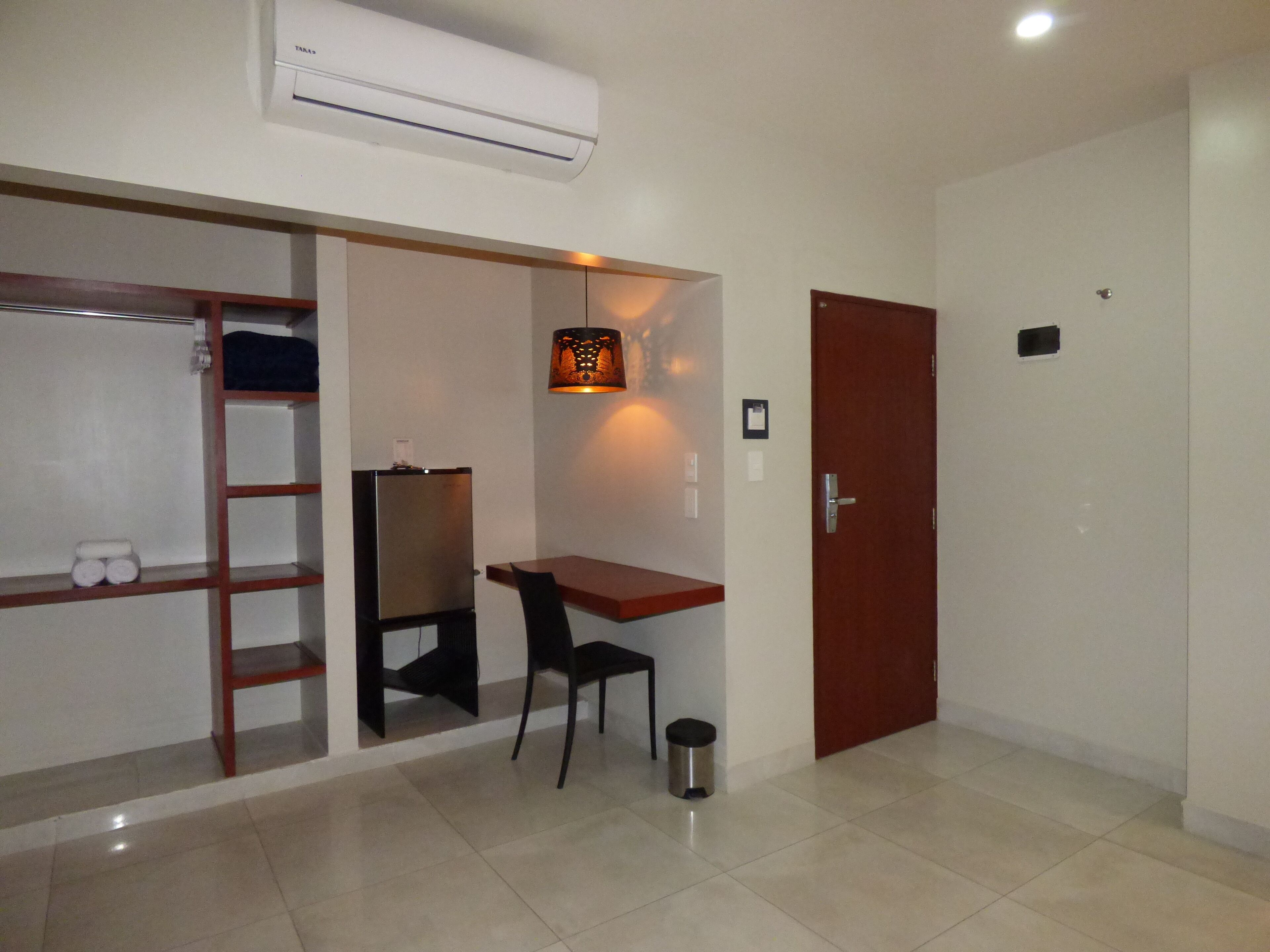 A room with a desk, chair, wardrobe, and an air conditioning unit.
