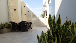 A paved outdoor area with a row of chairs, a planter with large-leafed plants, and a staircase leading to a higher level. - HOTEL OSHO (Santa Cruz)