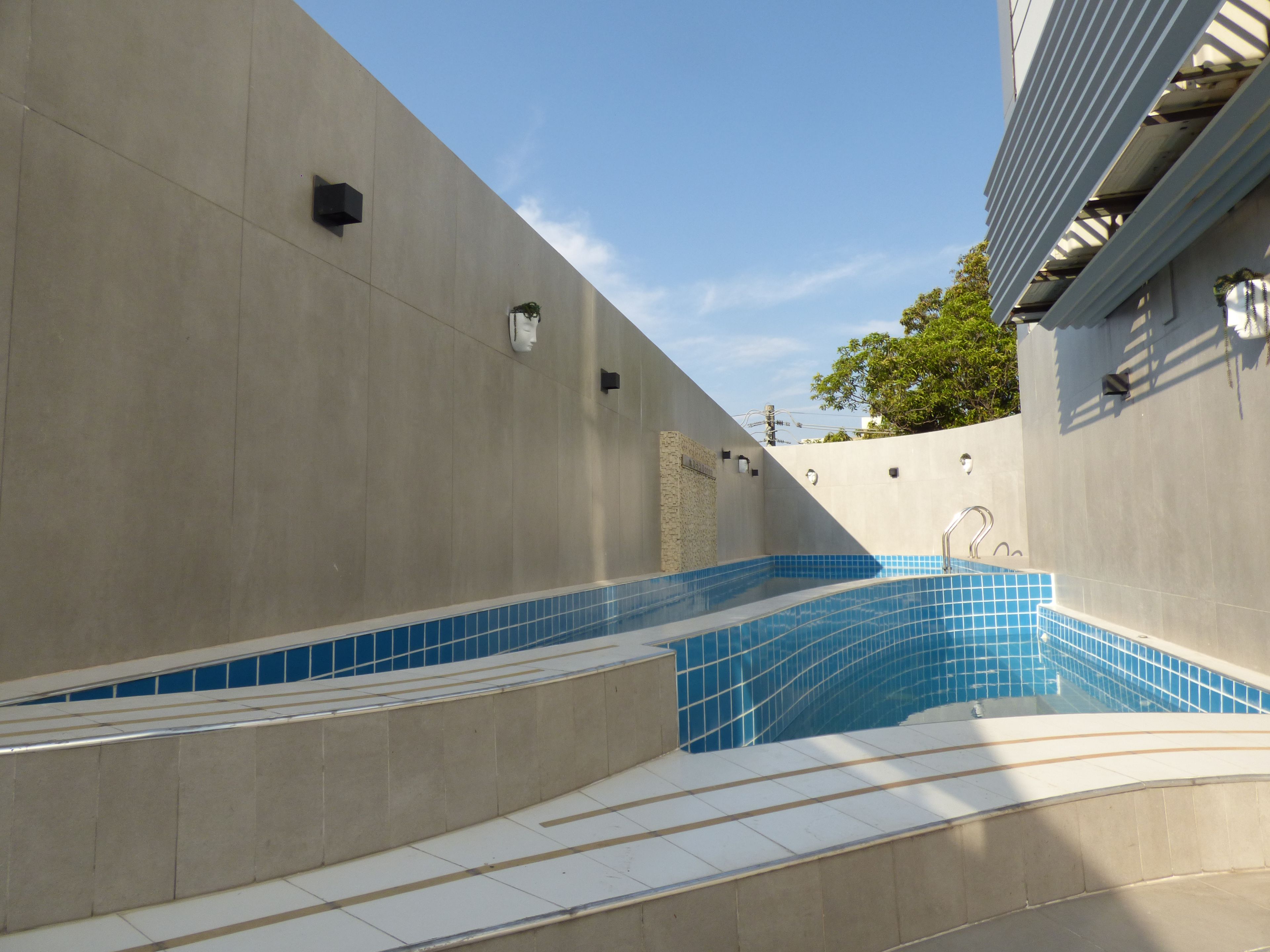 Una piscina con scalini d'accesso, circondata da un muro in cemento con bordo piastrellato.