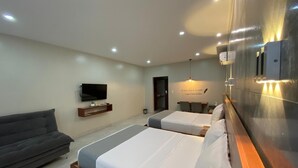 A hotel room with two beds, a sofa, a TV, and a wall-mounted light fixture. - HOTEL OSHO (Santa Cruz)