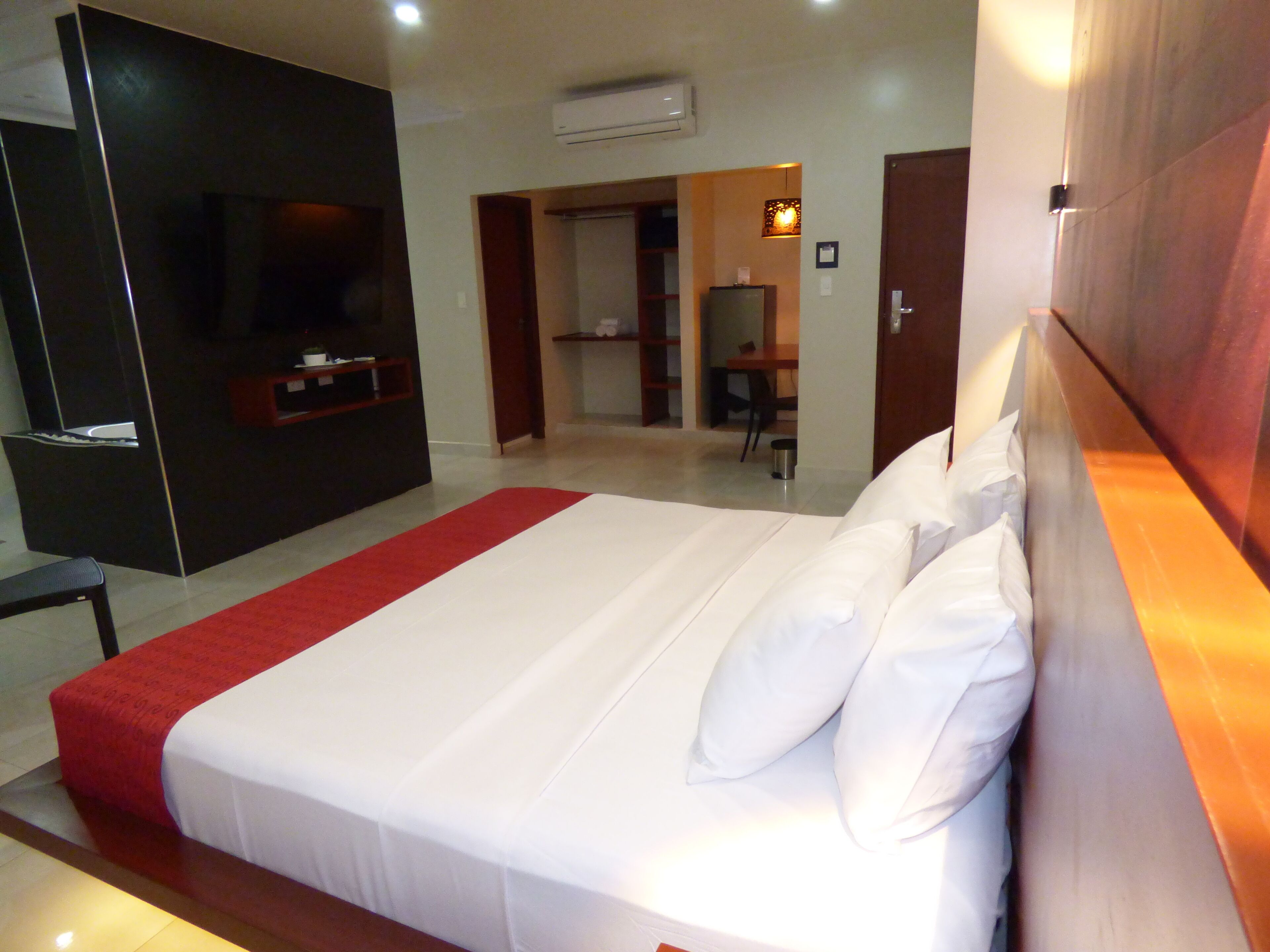 A hotel room with a large bed, a TV, a desk, and a bathroom visible through an open door.