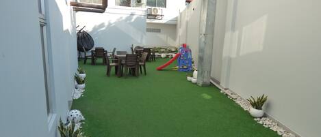 Un patio con césped artificial, una zona de juegos y un comedor.
