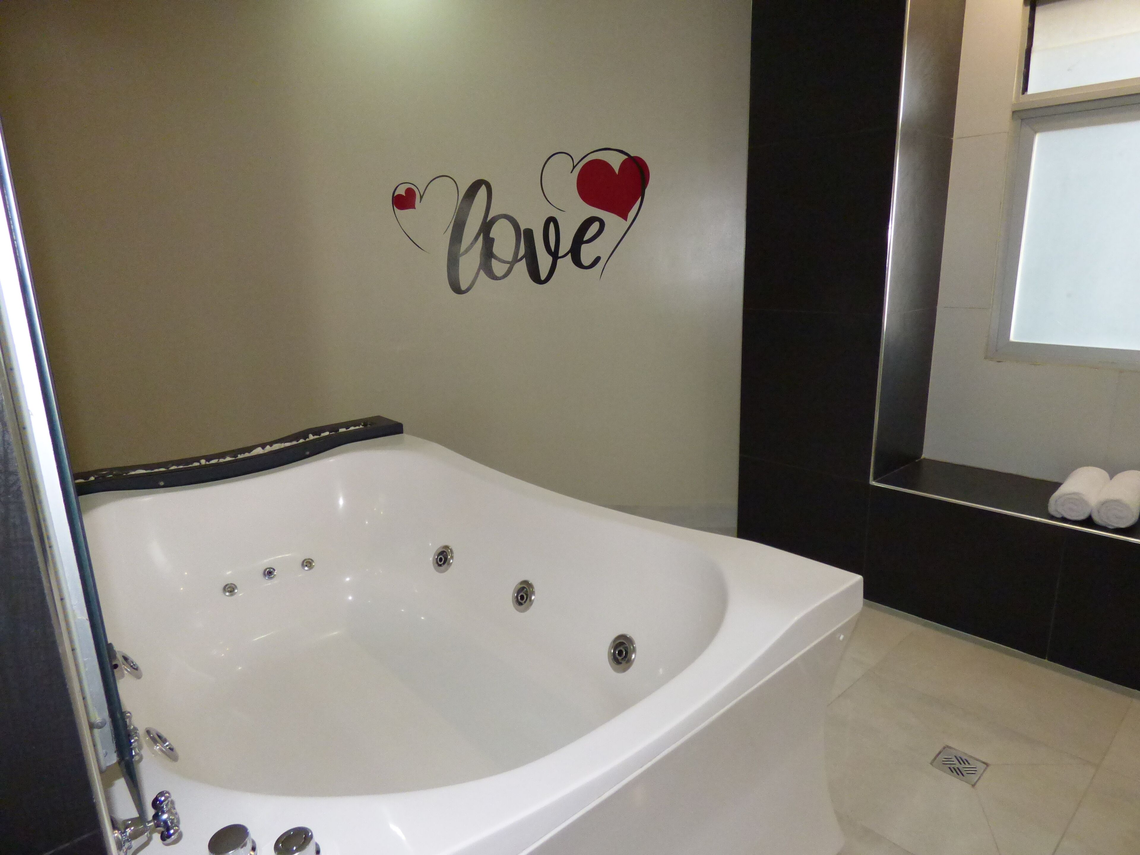 A modern bathroom with a white bathtub, a wall-mounted sign that says 'love,' and a window with a view.