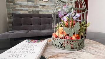 A modern living room with a grey sofa, a round table with a book, and a decorative metal birdcage with flowers.